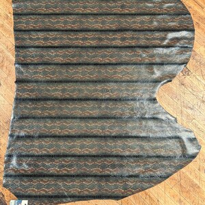 May include: A large piece of leather with a snakeskin pattern. The leather is primarily olive green and brown, with black horizontal stripes. The texture appears to be slightly glossy. The leather is irregularly shaped, with a small tag in the lower left corner.