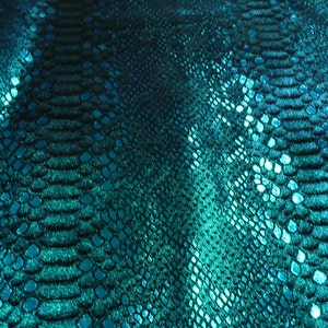以下が含まれることがあります： テクスチャ加工が施され、虹色に輝くターコイズ色のヘビ革生地。生地は控えめな光沢があり、鱗の模様が繰り返しパターンになっています。