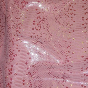 May include: Pink fabric with a snakeskin pattern and iridescent glitter. The fabric has a subtle sheen and a textured surface.