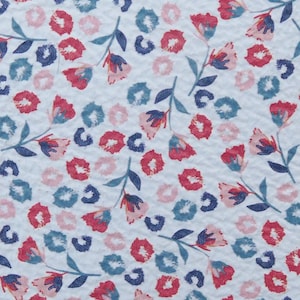 May include: White fabric with a repeating pattern of pink, red, and blue flowers. The flowers have a simple design with a single stem and three petals.