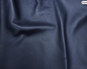 May include: A dark navy blue leather material with a natural grain texture. The surface features soft folds and drapes, creating subtle highlights and shadows across the matte finish of the hide, showcasing the flexible and smooth quality of the leather.