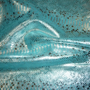 Könnte beinhalten: Türkisfarbener Stoff mit einem silbernen Schlangenhautmuster. Der Stoff ist glänzend und hat eine strukturierte Oberfläche.