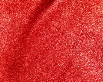 May include: Close-up of a textured, shiny red fabric. The material has a crinkled appearance, with highlights and shadows creating depth. The overall effect is a vibrant, eye-catching surface.