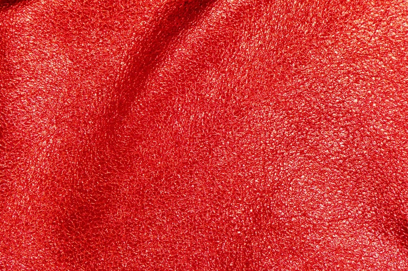 May include: Close-up of a textured, shiny red fabric. The material has a crinkled appearance, with highlights and shadows creating depth. The overall effect is a vibrant, eye-catching surface.