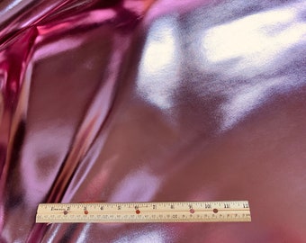 May include: A close-up of a pink metallic fabric with a ruler measuring 12 inches. The fabric has a subtle shimmer and a smooth texture.