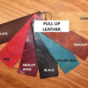 Peut inclure: Échantillon de cuir pull-up avec des couleurs variées : chocolat raisin, rouge, merlot, noir, vert d'eau, brandy et camel. Le texte "PULL UP LEATHER" est affiché sur un rectangle blanc.