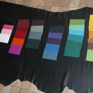 May include: A variety of leather swatches in different colors, including beige, pink, red, orange, purple, green, blue, brown, and yellow. The swatches are arranged in rows on a black surface.