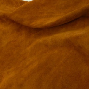 May include: A close-up of a piece of brown suede fabric. The fabric is soft and has a slightly textured surface.