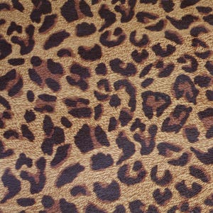 May include: Close-up of a fabric with a leopard print pattern. The design features dark brown spots on a tan background, creating a textured, animal-inspired aesthetic. The pattern is consistent across the fabric.
