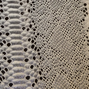 May include: Close-up of a silver snakeskin-textured fabric with a subtle shimmer. The fabric has a repeating pattern of scales.