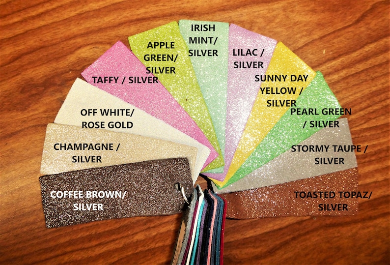 Op de afbeelding: Een kleurenkaart met glitterstofstalen met namen zoals "Ierse Munt/Zilver", "Appelgroen/Zilver", "Taffy/Zilver", "Wit/Roze Goud", "Champagne/Zilver", "Koffiebruin/Zilver", "Lila/Zilver", "Zonnige Dag Geel/Zilver", "Parelgroen/Zilver", "Stormachtig Taupe/Zilver" en "Geroosterde Topaas/Zilver".