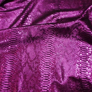 May include: Close-up of a vibrant, fuchsia-colored fabric with a snakeskin pattern. The material has a shiny, textured surface, with scales and folds visible throughout. The fabric appears to be draped, creating shadows and highlights.