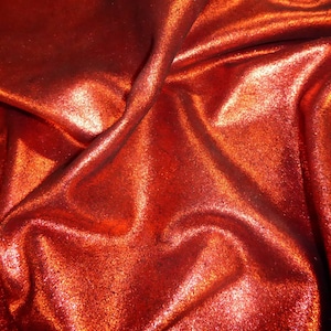 Puede incluir: Primer plano de una tela brillante y texturizada en un tono rojo vibrante. El material está drapeado, creando pliegues y reflejos suaves. La superficie tiene un aspecto brillante, captando la luz y añadiendo profundidad al color. Ideal para ropa o proyectos de manualidades.