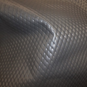 May include: Close-up of a dark grey quilted fabric with a diamond pattern. The fabric has a slightly shiny finish.