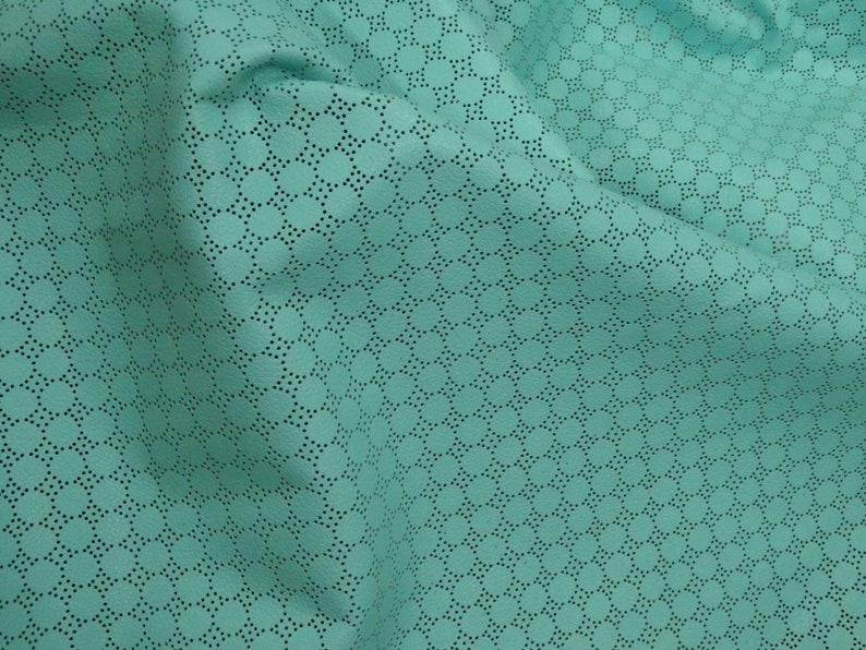 May include: Close-up of turquoise fabric featuring a repeating pattern of small, evenly spaced circles. The fabric has a perforated design, with tiny holes creating the pattern. The material is soft and appears draped, with visible folds and shadows.