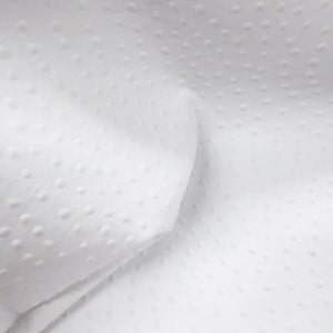 May include: White fabric with a textured, dotted pattern. The fabric is folded and has a soft, smooth texture.