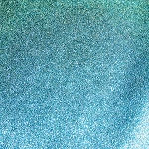 May include: Abstract textured background with a gradient of teal and turquoise. The surface has a rough, granular appearance, with light reflecting off the textured surface. The overall effect is a shimmering, iridescent look.