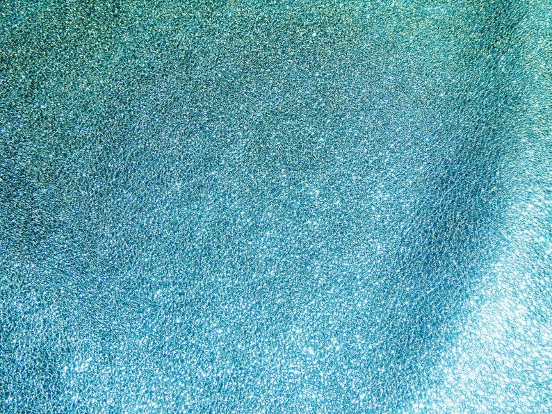 May include: Abstract textured background with a gradient of teal and turquoise. The surface has a rough, granular appearance, with light reflecting off the textured surface. The overall effect is a shimmering, iridescent look.