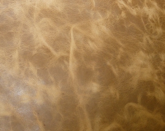 May include: A close-up view of a tan leather surface featuring a natural, distressed grain pattern. The texture displays light and dark brown variations with visible creases, wrinkles, and organic markings across the entire material surface.