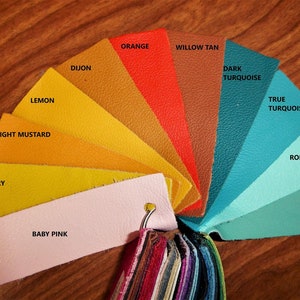 May include: A color chart with 10 leather swatches in various shades of yellow, orange, brown, turquoise, and blue. The swatches are labeled with the color names: Lemon, Light Mustard, Canary, Baby Pink, Dijon, Orange, Willow Tan, Dark Turquoise, True Turquoise, and Robin Egg.