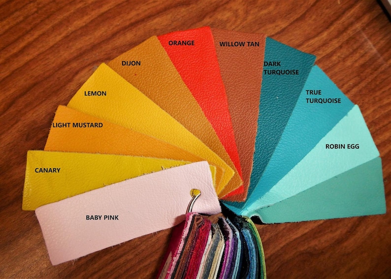 May include: A color chart with 10 leather swatches in various shades of yellow, orange, brown, turquoise, and blue. The swatches are labeled with the color names: Lemon, Light Mustard, Canary, Baby Pink, Dijon, Orange, Willow Tan, Dark Turquoise, True Turquoise, and Robin Egg.