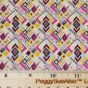May include: A close-up of a fabric with a geometric pattern in shades of pink, yellow, blue, and gray. The fabric is measured with a ruler, showing a length of 12 inches.