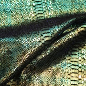 May include: Close-up of a textured fabric with a snakeskin pattern. The fabric features a blend of teal, green, and black colours, with a subtle sheen. The pattern is detailed with small, scale-like shapes.