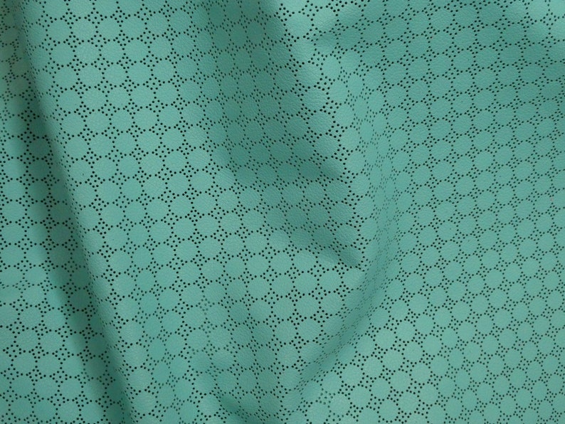 May include: Close-up of a teal fabric with a perforated pattern. The fabric has a soft texture and is draped, showing the intricate design of small, evenly spaced holes arranged in a repeating circular pattern.