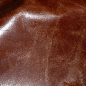 May include: Close-up of a brown leather texture with a smooth, shiny surface and subtle wrinkles.