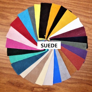 May include: A circular arrangement of suede fabric swatches in various colors, including red, pink, teal, and black. The word "SUEDE" is displayed in a white rectangle at the center of the swatches. The swatches are arranged on a wooden surface.