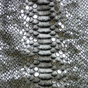 Könnte beinhalten: Nahaufnahme eines silbernen und schwarzen Schlangenlederstoffs mit einem strukturierten Muster.