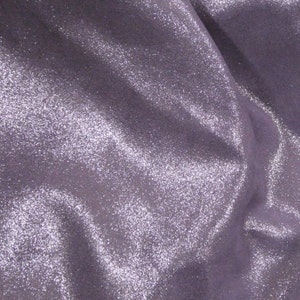Puede incluir: Primer plano de una tela brillante de color lavanda. El material tiene una textura suave y fluida con un brillo sutil. La tela está reunida en pliegues suaves, creando sombras y reflejos.