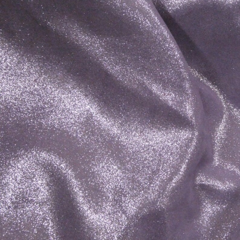 Puede incluir: Primer plano de una tela brillante de color lavanda. El material tiene una textura suave y fluida con un brillo sutil. La tela est&aacute; reunida en pliegues suaves, creando sombras y reflejos.