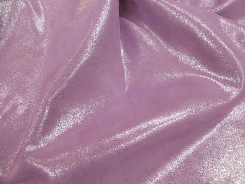 May include: A close-up of a shimmering, lavender fabric. The material has a soft, flowing texture with subtle highlights, creating a lustrous appearance. The fabric's folds and curves add depth and dimension to the image.