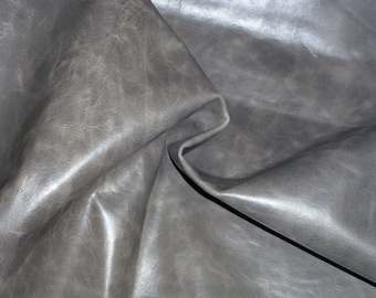 May include: Close-up of a piece of grey leather with a textured surface. The leather is folded and has a soft, supple look.