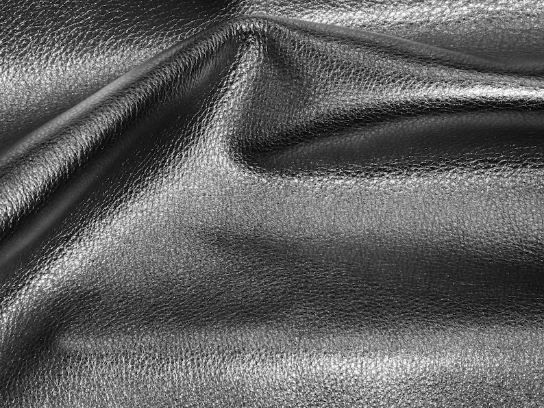 May include: Close-up of a silver leather fabric with a textured surface. The fabric is folded and draped, creating soft folds and wrinkles.