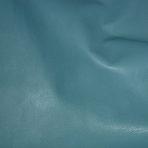 May include: A close-up of a textured, teal blue fabric. The fabric has a slightly grainy texture and is folded in the center.