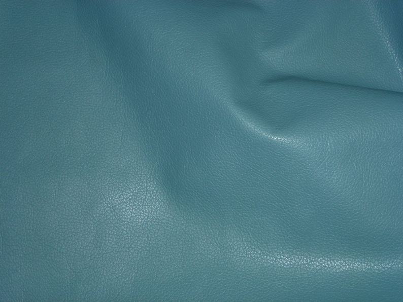 May include: A close-up of a textured, teal blue fabric. The fabric has a slightly grainy texture and is folded in the center.