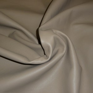 May include: A close-up of a piece of light brown leather fabric. The fabric is smooth and has a slight sheen.