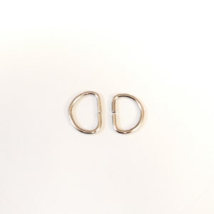 May include: Two silver metal D-rings, commonly used for attaching straps or chains to bags, belts, or other items.