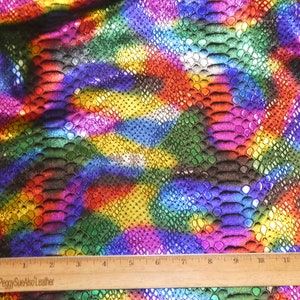 May include: A close-up of iridescent rainbow coloured fabric with a snakeskin pattern. A wooden ruler with the text "PeggySueAlsoLeather" is in the bottom of the image.