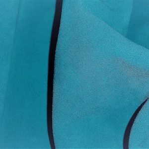 May include: Close-up of a teal blue fabric with a black seam running down the center. The fabric is textured and has a slight sheen.
