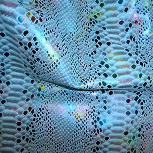 May include: Close-up of a white iridescent snakeskin fabric with a textured pattern. The fabric has a subtle shimmer and a light blue hue.