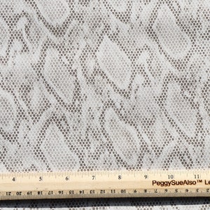 May include: White fabric with a brown and white camouflage pattern. The fabric has a small, repeating circle pattern. A ruler is visible at the bottom of the image, showing measurements in inches.