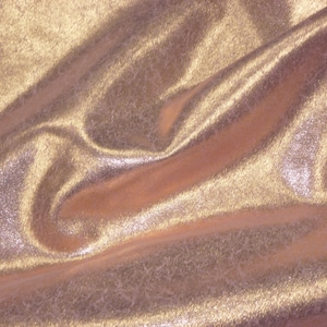 K&ouml;nnte beinhalten: Nahaufnahme eines glatten, metallischen Stoffes mit einem subtilen Schimmer. Der Stoff ist hellgoldfarben und hat eine weiche, flie&szlig;ende Textur.
