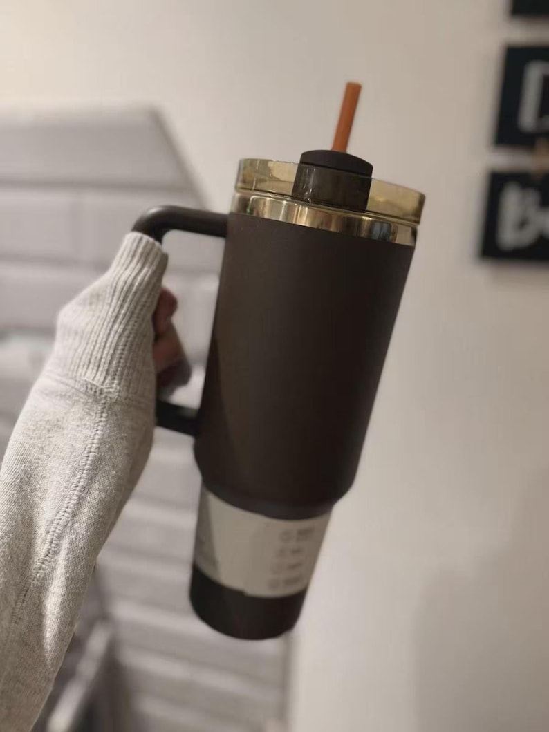 Puede incluir: Un vaso t&eacute;rmico de color marr&oacute;n oscuro con asa a juego y tapa transl&uacute;cida de color &aacute;mbar. El vaso presenta una base delgada y c&oacute;nica e incluye una pajita naranja recta insertada a trav&eacute;s del centro de la tapa para poder beber.