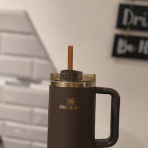 Puede incluir: Un vaso Stanley de color marr&oacute;n oscuro con asa a juego, tapa transparente y pajita marr&oacute;n. El logotipo de Stanley est&aacute; impreso en dorado en la parte frontal. El vaso tiene un cuerpo cil&iacute;ndrico y un asa lateral resistente para sujetarlo.