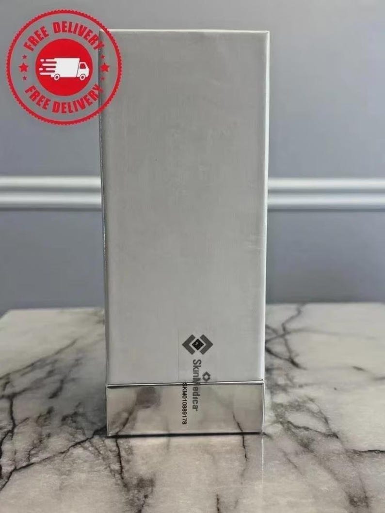 May include: A rectangular white product box with a metallic silver base. The box features a small black logo and the text SkinMedica printed vertically near the bottom, along with the alphanumeric code SKM010889178 printed below the brand name.