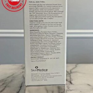 May include: A white rectangular box of SkinMedica TNS Advanced+ Serum. The front features black text detailing product benefits, directions, and ingredients. A silver metallic base is at the bottom. A red circular free delivery stamp is in the corner.