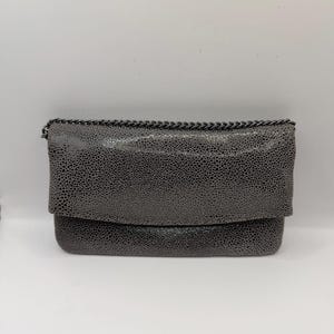 May include: A grey clutch bag with a textured finish and a chain strap. The bag features a fold-over flap and a dark grey chain. The clutch is a neutral colour and suitable for various occasions.